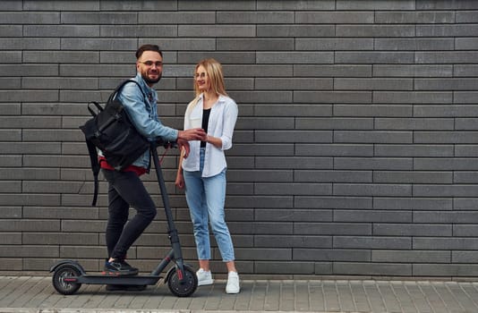 With electric schooter. Young stylish man with woman in casual clothes outdoors together. Conception of friendship or relationships.