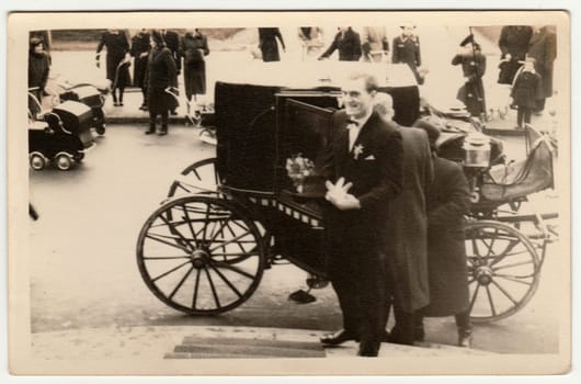 THE CZECHOSLOVAK REPUBLIC - CIRCA 1940s: Vintage photo shows a groom. A historical carriage - coach is on the background and historical prams too. Retro black and white photography. Circa 1940s.