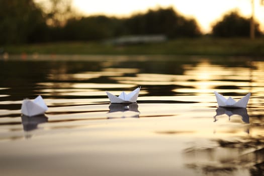 three paper boats floating on the waves in the water at a beautiful sunset. homemade Origami boats on the water surface in the evening. Close-up