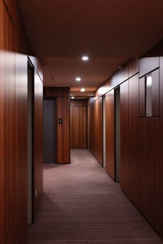 Empty dark interior of the modern Hotel corridor, with wood-paneled walls, elegant carpets and lighting on the ceiling