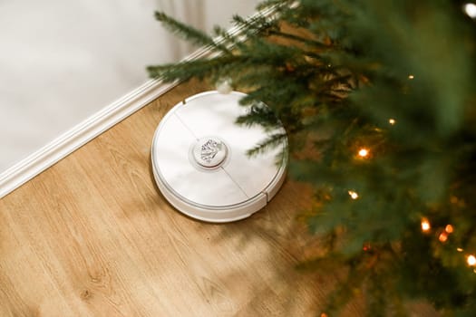 Smart home. Robot vacuum cleaner performs automatic cleaning. Cleans the parquet from Christmas tree needles after the new year. cleans near the Christmas tree after the holidays