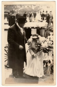 THE CZECHOSLOVAK REPUBLIC - CIRCA 1940s: Vintage photo shows a groom - bridegroom and bride. A historical carriage - coach is on the background. Retro black and white photography. Circa 1940s.