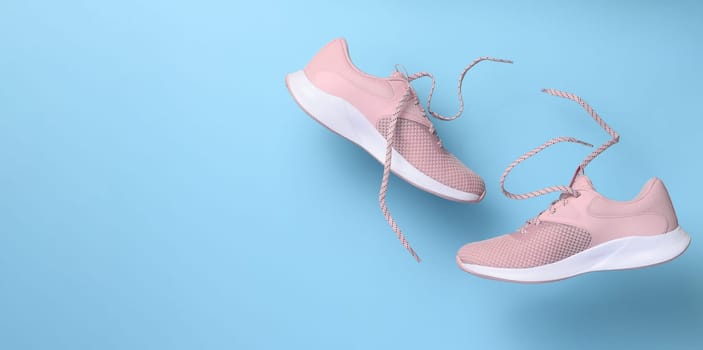 Pink women's sports sneakers with laces levitate on a blue background. Copy space