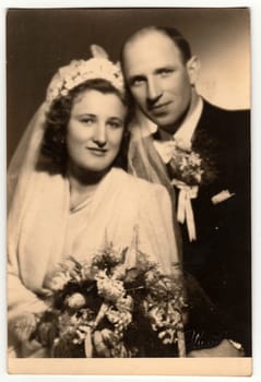 ZLIN, THE CZECHOSLOVAK REPUBLIC - MARCH 17, 1944: Vintage photo shows newlyweds pose after wedding ceremony. Retro black and white studio photography. Circa 1940s.