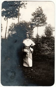 THE CZECHOSLOVAK REPUBLIC - CIRCA 1930s: Vintage photo shows woman wears white dress and she holds ladies hat - cloche hat. The woman poses outdoors. Retro black and white photography.