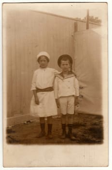 HAMBURG, GERMANY (DEUTSCHES REICH) - NOVEMBER 13, 1917: Vintage photo shows siblings - girl and boy pose in the backyard. Boy wears a sailor costume and girl wears a white dress. Retro black and white photography.