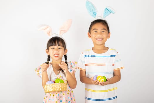 Happy Easter Day. Two smile Asian little girl and boy wearing easter bunny ears holding basket with eggs isolated on white background with copy space, Happy family children in holiday