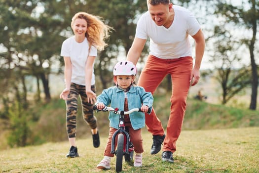 Mother and father teaching daughter how to ride bicycle outdoors.