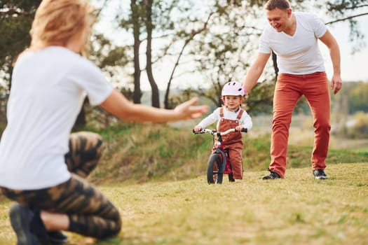 Mother and father teaching daughter how to ride bicycle outdoors.