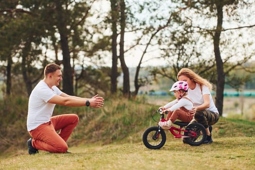 Mother and father teaching daughter how to ride bicycle outdoors.