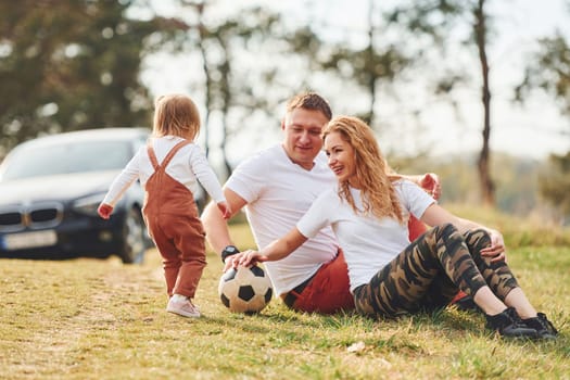 Playing with soccer ball. Father and mother spending weekend outdoors near forest with daughter.