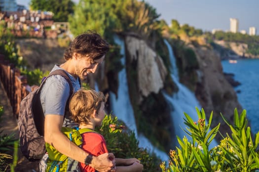 Father and son tourists on the background of Duden waterfall in Antalya. Famous places of Turkey. Lower Duden Falls drop off a rocky cliff falling from about 40 m into the Mediterranean Sea in amazing water clouds. Tourism and travel destination photo in Antalya, Turkey. Turkiye.