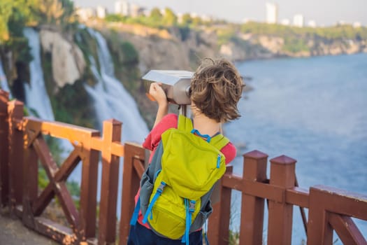 Boy tourist with a backpack on the background of Duden waterfall in Antalya. Famous places of Turkey. Lower Duden Falls drop off a rocky cliff falling from about 40 m into the Mediterranean Sea in amazing water clouds. Tourism and travel destination photo in Antalya, Turkey. Turkiye.