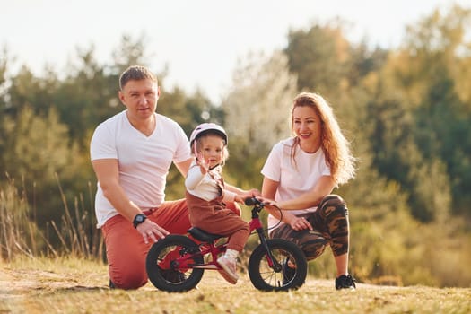 Mother and father teaching daughter how to ride bicycle outdoors.