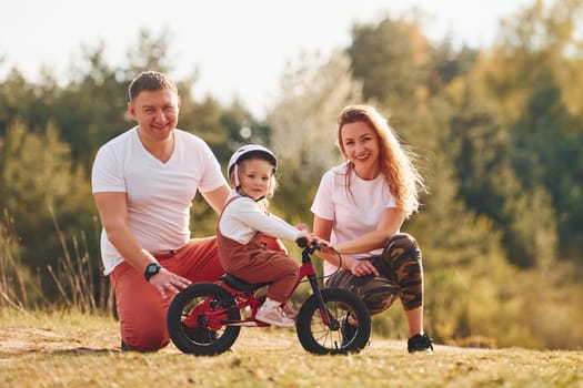 Mother and father teaching daughter how to ride bicycle outdoors.