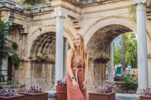 Happy female tourist traveler discover interesting places and popular attractions and walks in the old city of Antalya. Hadrian Kapisi turkey landmark city history. Popular tourist attraction - ancient Roman Hadrian Gate in old town Antalya, Turkey on a summer day. Turkiye.