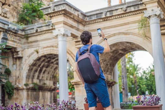 Happy male tourist traveler discover interesting places and popular attractions and walks in the old city of Antalya. Hadrian Kapisi turkey landmark city history. Popular tourist attraction - ancient Roman Hadrian Gate in old town Antalya, Turkey on a summer day. Turkiye.