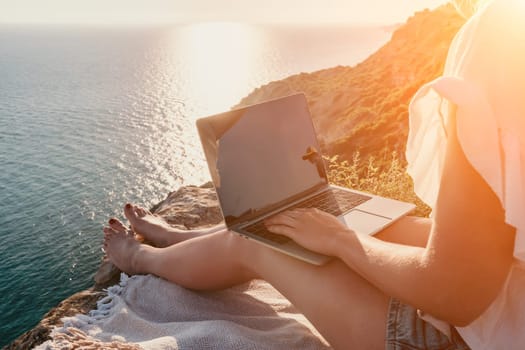 Woman sea laptop. Business woman in yellow hat working on laptop by sea. Close up on hands of pretty lady typing on computer outdoors summer day. Freelance, digital nomad, travel and holidays concept.