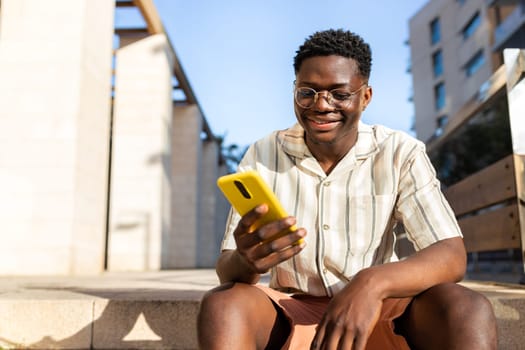 Young African American man using mobile phone outdoors sitting on stairs. Copy space. Lifestyle concept.