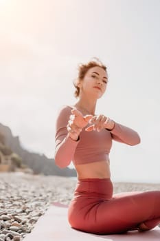 Young woman with long hair in white swimsuit and boho style braclets practicing outdoors on yoga mat by the sea on a sunset. Women's yoga fitness routine. Healthy lifestyle, harmony and meditation