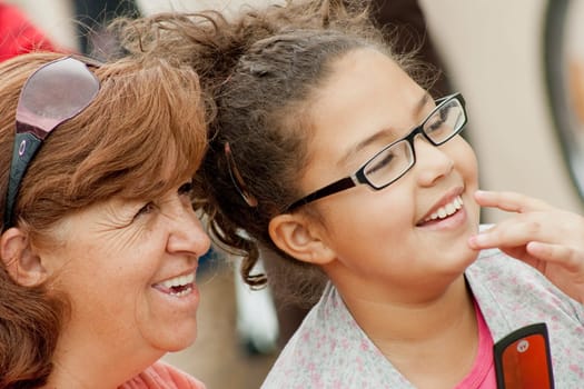 closeup of a mother and daughter in the street together smiling and looking at the same place. the two people are wearing glasses