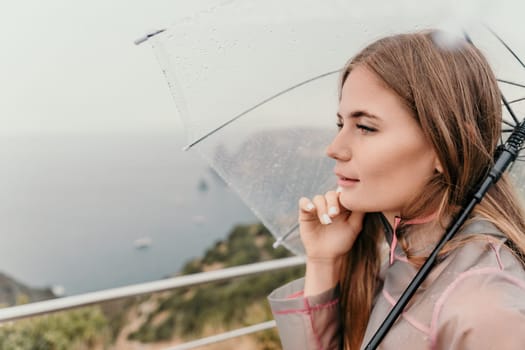 Woman rain park. Happy woman portrait wearing a raincoat with transparent umbrella outdoors on rainy day in park near sea. Girl on the nature on rainy overcast day