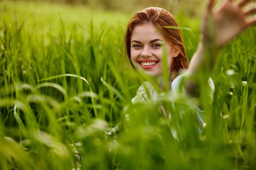 portrait of a broadly smiling woman sitting in tall grass and holding out her hands to the camera. High quality photo