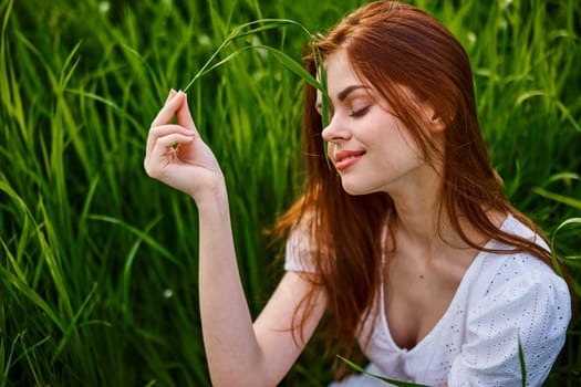 portrait of a cute red-haired woman sitting in tall grass and holding a leaf in her hands. High quality photo