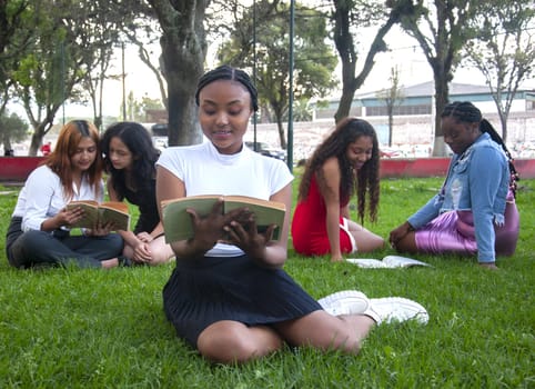 pretty young black woman reading a book in a park surrounded by friends from her college. eading books with friends on book day and sant jordi