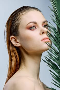 beauty portrait of a beautiful, elegant woman standing holding a palm leaf near her face, looking away. Vertical photo without retouching of problem skin. High quality photo