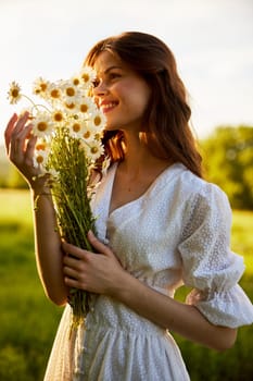 close-up portrait of a woman in a light dress in a field during sunset with a bouquet of daisies in her hands in backlight. High quality photo