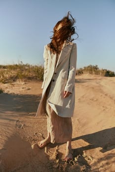 an atypical portrait of a woman in stylish summer clothes stands on the sands with hair covering her face. High quality photo