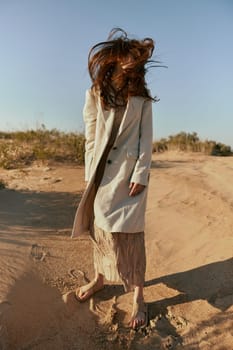 an atypical portrait of a woman in stylish summer clothes stands on the sands with hair covering her face. High quality photo