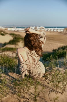 red-haired woman posing while sitting with her back to the camera holding her hair with her hand on the sea coast. High quality photo