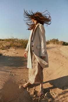 an atypical portrait of a woman in stylish summer clothes stands on the sands with hair covering her face. High quality photo