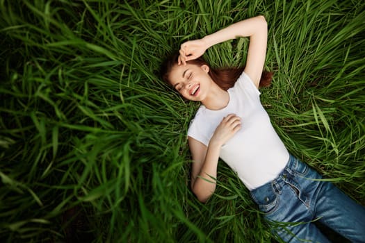 a beautiful, slender woman lies in the tall green grass in a white T-shirt. High quality photo