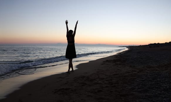 Woman with her hands up on beach at sunset back view. Happiness and outdoor recreation concept