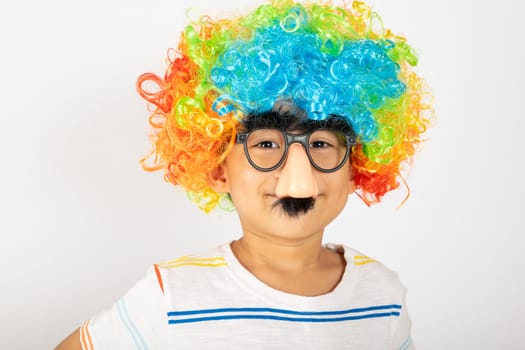 April Fool's Day. Portrait of Funny kid boy clown wears a curly wig colorful a big nos and glasses and has a mustache isolated on white background with copy space, Happy child festive decor