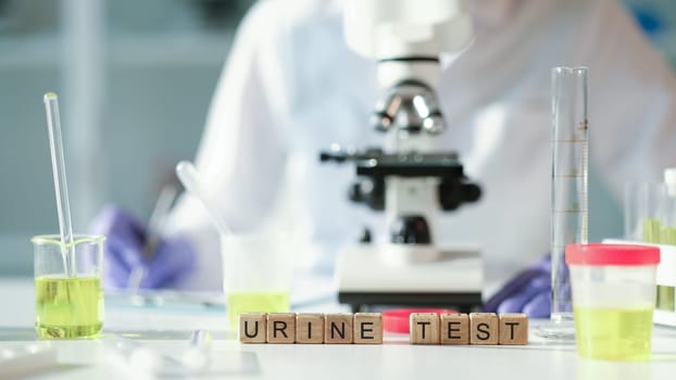 Word urine test on wooden cubes against background of microscope and jars in lab closeup. Laboratory diagnosis of diseases of urinary system concept