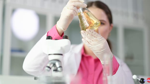 Scientist chemist looking at flask with yellow brake oil in chemistry lab closeup. Quality control of petroleum products concept