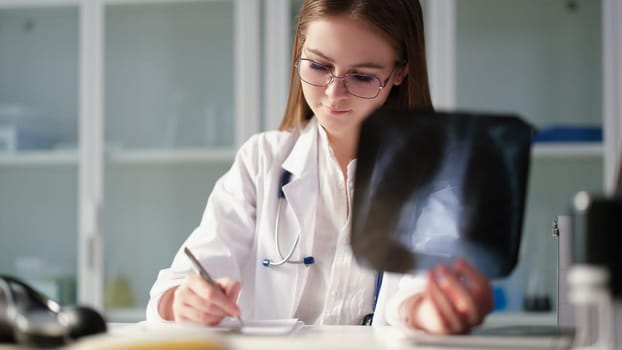 Therapist doctor holding xray of lungs in hands and writing in medical documents in clinic. Diagnosis and treatment of pneumonia and lung cancer concept