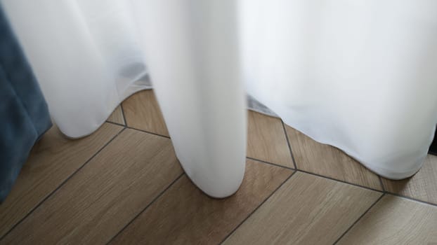 White curtain touching floor with parquet board at home closeup. Interior design concept