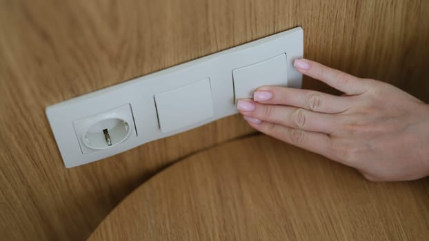 Hand pressing light switch in wall of house closeup. Saving electricity concept