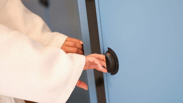 Women hands in bathrobe opening doors of blue wardrobe at home closeup. Clothes storage comfortable furniture and fittings concept