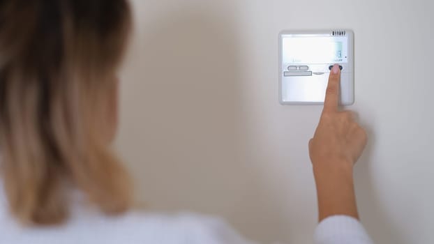 Woman pressing button on remote control of air conditioner in wall closeup. Comfortable temperature at home concept