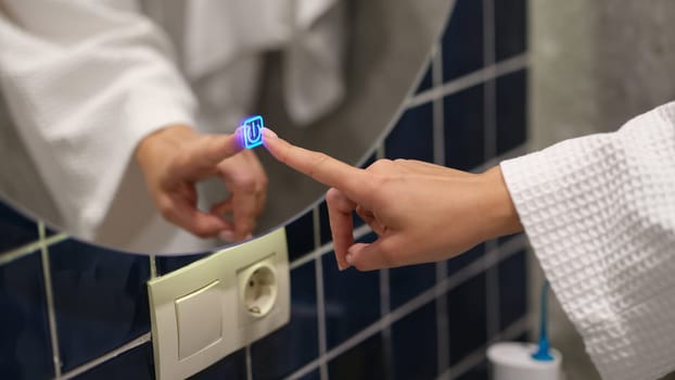 Woman hand pressing button for turning on light and heating mirror in bathroom closeup. Modern home accessories concept