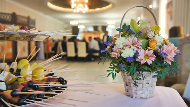Wedding celebration background concept. A bouquet of flowers and fruits on the background of the banquet guests who are eating