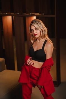 a beautiful girl dressed in a red formal suit posing in a modern interior.