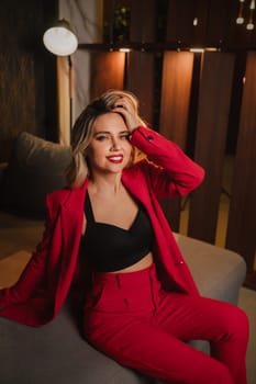 a beautiful girl dressed in a red formal suit posing in a modern interior.