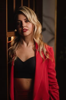 a beautiful girl dressed in a red formal suit posing in a modern interior.